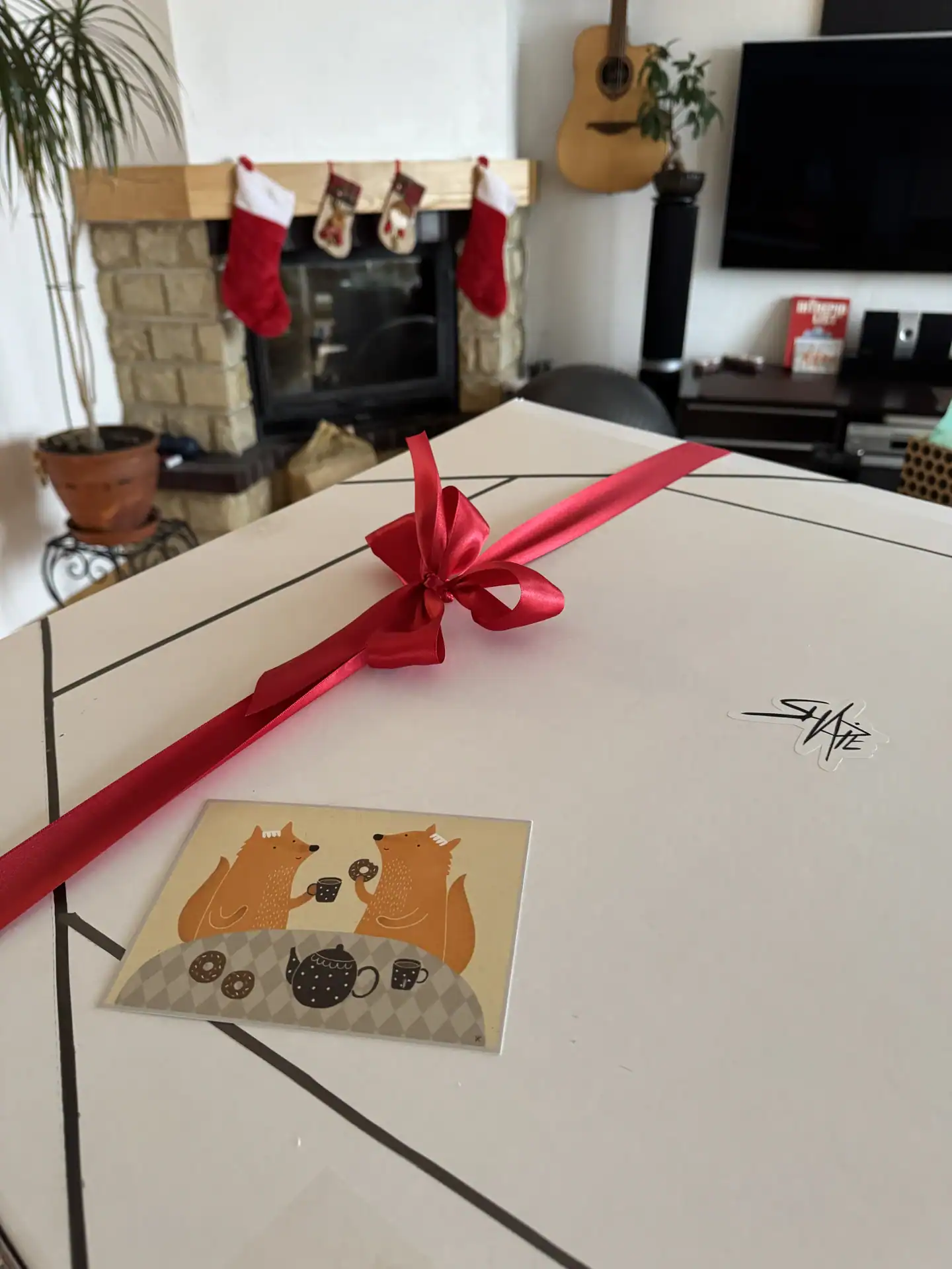 Shapie artwork gift box tied with a red ribbon, with an illustrated greeting card beside the logo