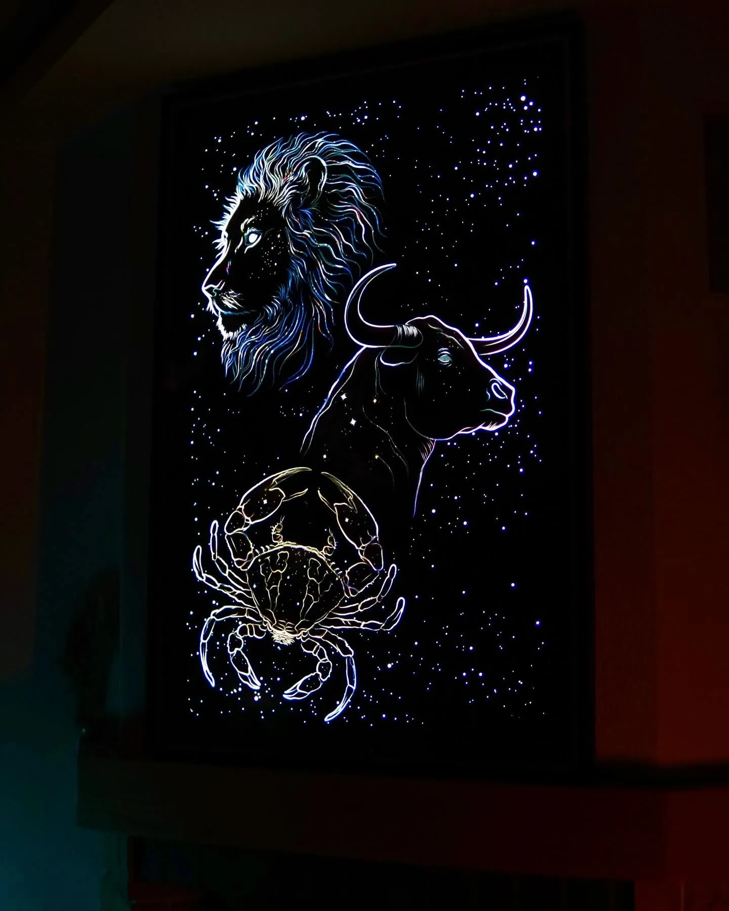 The same zodiac artwork at night, with illuminated lion, bull and crab outlines and bright star details.